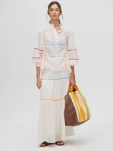 Falda larga blanca confeccionada en broderie de algodón con diseño de paneles escalonados, detalles de galones con transparencias en color azul y naranja, y pretina elástica con cordón ajustable.