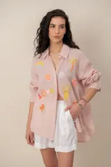 Camisa de lino rosada con mangas largas, cuello camisero y bordados coloridos de motivos veraniegos repartidos en el frente.