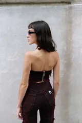 Top halter de denim con efecto lavado en tonos rojizos y negros. Presenta un diseño entallado con recortes frontales, terminaciones desflecadas y un aplique metálico decorativo en el centro del escote.