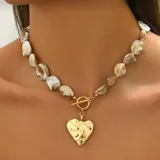 Collar corto con cuentas irregulares color crema y dije de corazón dorado con textura irregular.