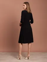 Vestido midi negro de RM Richards en seda fría, con escote en V, mangas 3/4, frunce en la delantera y aplique circular de brillos en el centro.