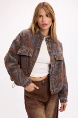 Campera de jean con diseño de estampado paisley en tonos marrones y grises. Presenta un corte relajado, cuello camisero, cierre frontal con botones metálicos y bolsillos frontales con solapa.