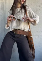 Blusa beige de corte oversize, con mangas largas, botones forrados en el frente y detalles de puntillas y alforzas verticales.