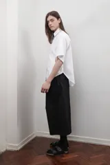 Camisa blanca oversize de popelina de algodón, con cuello clásico, manga corta amplia, bolsillo frontal y canesú en la espalda con pliegue central.