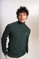 Sweater de punto acanalado en color verde oscuro, con cuello alto y cierre frontal parcial de un cuarto. Presenta puños y ruedo elásticos, con el logo de la marca bordado en el pecho.