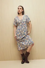 Vestido largo celeste con estampado floral en tonos beige y marrón, escote en V con botones al frente, mangas cortas y falda con leve vuelo. Confeccionado en viscosa liviana.