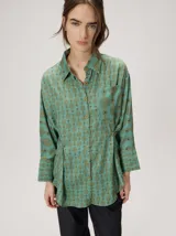 Camisa holgada de algodón liviano, con estampado geométrico de estilo retro en tonos verdes, cuello camisero y bolsillo frontal.