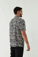 Camisa de manga corta con cuello cubano, confeccionada en viscosa con estampado de hojas en tonos azules. Presenta cierre frontal abotonado y corte slim.