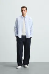 Camisa celeste a rayas verticales, de corte relaxed fit, confeccionada en lino y algodón. Tiene cuello abotonado, manga larga con puños abotonados, bolsillo de parche en el pecho y cierre frontal con botones.