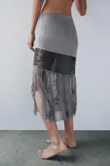 Falda midi de tiro medio, color gris, confeccionada en mezcla de lyocell y viscosa, con detalle de apliques de lentejuelas y bajo de tejido transparente plisado con bordados florales.