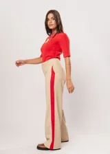 Pantalón beige de tiro alto con bolsillos delanteros y traseros, cierre frontal con cremallera y botón, y detalle de pespuntes rojos en los laterales.