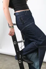 Jean recto de denim azul oscuro con cortes horizontales y trenzados laterales con cordones ajustables. Cuenta con ajuste en la parte trasera de la pretina.