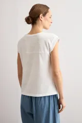 Remera mostaza de manga corta con detalles de encaje bordado (broderie) en los hombros, cuello redondo y corte recto.