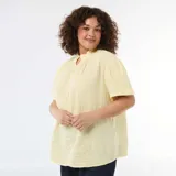 Blusa de gasa de algodón color amarillo pastel, con cuello alto fruncido, cierre frontal parcial con botones y mangas cortas abullonadas.