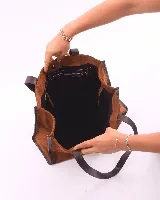 Bolso tipo shopper de gran tamaño, confeccionado en cuero gamuzado color marrón. Presenta estructura rectangular con bordes reforzados en cuero liso oscuro, doble asa de hombro y cierre mediante botón magnético.