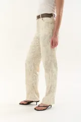 Pantalón de jean tiro medio, color crema o blanco roto, con estampado sutil en tono grisáceo. Corte recto o ligeramente acampanado.