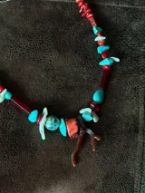 Collar corto elaborado con cuentas de turquesa reconstituida, piezas de nácar blanco, cuentas de cristal rojo y turquesa, y un dije central con forma de rama de coral.