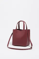 Bolso pequeño de piel color borgoña, con estructura rígida y forma de cubo. Posee doble asa de mano y una correa larga para llevar al hombro o cruzado. El frente lleva el logo metálico de Bimba y Lola.