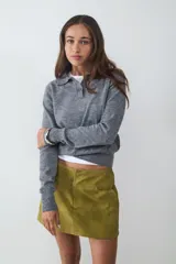 Pollera mini color verde oliva con efecto desgastado, dos bolsillos delanteros y cierre oculto. Confeccionada en tejido plano.