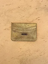 Tarjetero de cuero color dorado con acabado brillante, cuenta con ranuras para tarjetas y placa metálica con logo de la marca.
