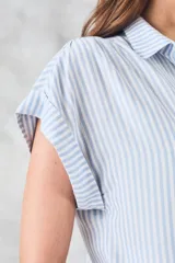 Blusa de viscosa rayada en blanco y celeste, con cuello camisero, mangas cortas con dobladillo y botones frontales.