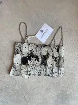Top de diseño artesanal confeccionado en cuero vacuno con estampado animal print tipo vaca. La prenda está formada por piezas rectangulares unidas mediante argollas metálicas y cuenta con breteles de cadena plateada.
