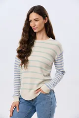 Buzo tejido de algodón con diseño a rayas horizontales, cuello redondo y mangas largas. El cuerpo presenta rayas en tonos azul y beige, mientras que las mangas combinan rayas en tonos azul y rosado.