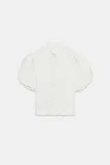 Blusa de cuello redondo con detalle de volados, manga corta abullonada con terminación elástica y cierre frontal con botones. Presenta un diseño de tejido plisado en toda la prenda.
