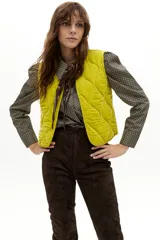 Chaleco capitoneado de terciopelo de seda, con cuello a la base y diseño sin mangas. Presenta un acabado acolchado con costuras onduladas y un tono amarillo vibrante.