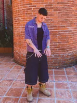 Camisa de manga corta con corte híbrido boxy fit/oversize, confeccionada en algodón. Disponible en tres diseños: a cuadros marrones, a rayas blancas y negras, y a rayas burdeos y blancas. Presenta bordados de diseño propio de la marca.