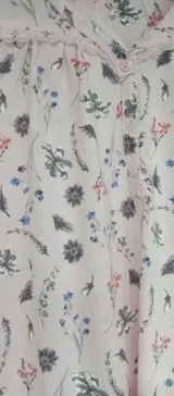 Camisón sin mangas de corte recto y largo midi, con cuello redondo y detalle de botones frontales. Presenta un estampado floral en tonos suaves sobre fondo rosado.