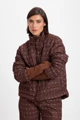 Campera de abrigo con cuello alto y cierre frontal con botones a presión. Presenta un diseño capitoneado con estampado geométrico en tonos marrones, mangas largas con puños internos de tejido acanalado y bolsillos frontales.