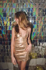 Vestido corto de fiesta color plateado con acabado brillante. Presenta un diseño de dos piezas que simula un conjunto de top y pollera, con aberturas laterales en la cintura, escote en V y tirantes finos que se cruzan en la espalda.