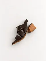 Sandalias de cuero marrón con punta cuadrada, tiras cruzadas y hebilla metálica grande en el empeine. Poseen taco ancho de madera de altura media.