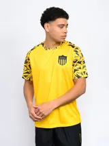 Remera deportiva de entrenamiento color amarillo, con cuello redondo y mangas cortas. Las mangas presentan un estampado geométrico en tonos de negro y gris. Lleva un escudo bordado en el pecho.