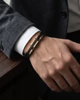 Pulsera masculina con diseño de placa central en acero con baño de oro rosa y detalles en negro, montada sobre una correa de cuerina negra con textura.