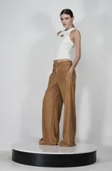 Pantalón de tiro alto color marrón, de corte ancho y silueta fluida, confeccionado en tela satinada. Presenta un detalle de ojalillos metálicos y cordón en la cintura, con bolsillos laterales.