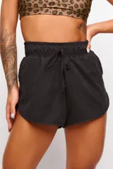 Short deportivo negro de tejido suave, con cintura elástica fruncida y lazo ajustable al frente. Presenta un corte redondeado en el ruedo.