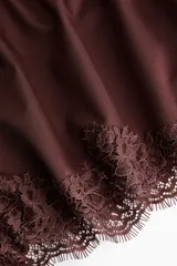 Bombacha tipo shortie de tiro alto, confeccionada en tela satinada color marrón oscuro, con terminación de encaje floral en el ruedo inferior.