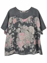 Blusa de manga corta color azul jean con diseño floreado en tonos rosados y grises, escote redondo y detalle de calados en forma de V en el pecho.