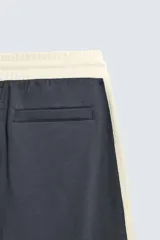 Pantalón jogger de corte wide fit en tejido compacto color gris oscuro. Presenta cintura elástica con cordón ajustable, bandas laterales en contraste color beige y costuras frontales tipo pinza.