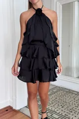 Top negro con escote halter y detalle de rosa de tela removible en el cuello. Presenta tres volados que le dan movimiento.