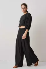 Pantalón largo negro de corte ancho y holgado, con bolsillos laterales y detalle de bordado calado en el ruedo.