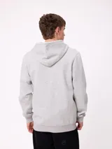 Campera canguro de felpa color gris claro melange, con capucha ajustable mediante cordones negros, cierre frontal completo, bolsillos tipo canguro y parche con logo de la marca en el pecho.