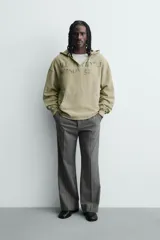 Sudadera de corte relajado color verde oliva con efecto lavado. Presenta capucha con abertura frontal, bolsillo tipo canguro, mangas largas con puños de rib y bajo con acabado irregular. Incluye estampado frontal con texto.