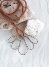 Colgante con cordón de cuero marrón y dije de alpaca plateada con forma de flor.