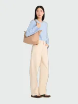 Bolso tote de tamaño mediano, diseño minimalista en color beige, con asas cortas para llevar al hombro y cierre superior.