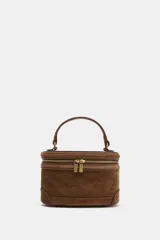 Bolso formato vanity de gamuza color marrón, con asa de mano superior y correa bandolera extraíble y ajustable. Presenta cierre de doble cremallera metálica dorada y detalles de pespuntes en el cuerpo.