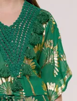Blusa verde de gasa con transparencia y estampado metalizado dorado, de silueta holgada y mangas cortas. Presenta escote en V con pechera tejida en crochet y apliques de borlas colgantes.