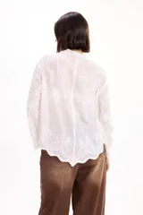 Camisa blanca de manga larga con cuello clásico y cierre frontal de botones. Presenta un delicado diseño bordado floral en toda la prenda con detalles calados.
